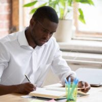 Serious african man university student studying reading textbook making notes