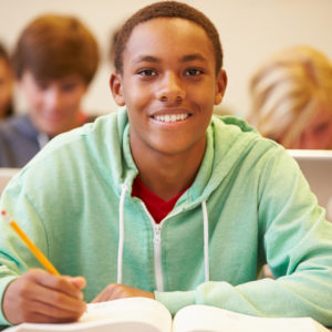 Male High School Student Studying At Desk In Classroom Male High School Student Studying At Desk In Classroom